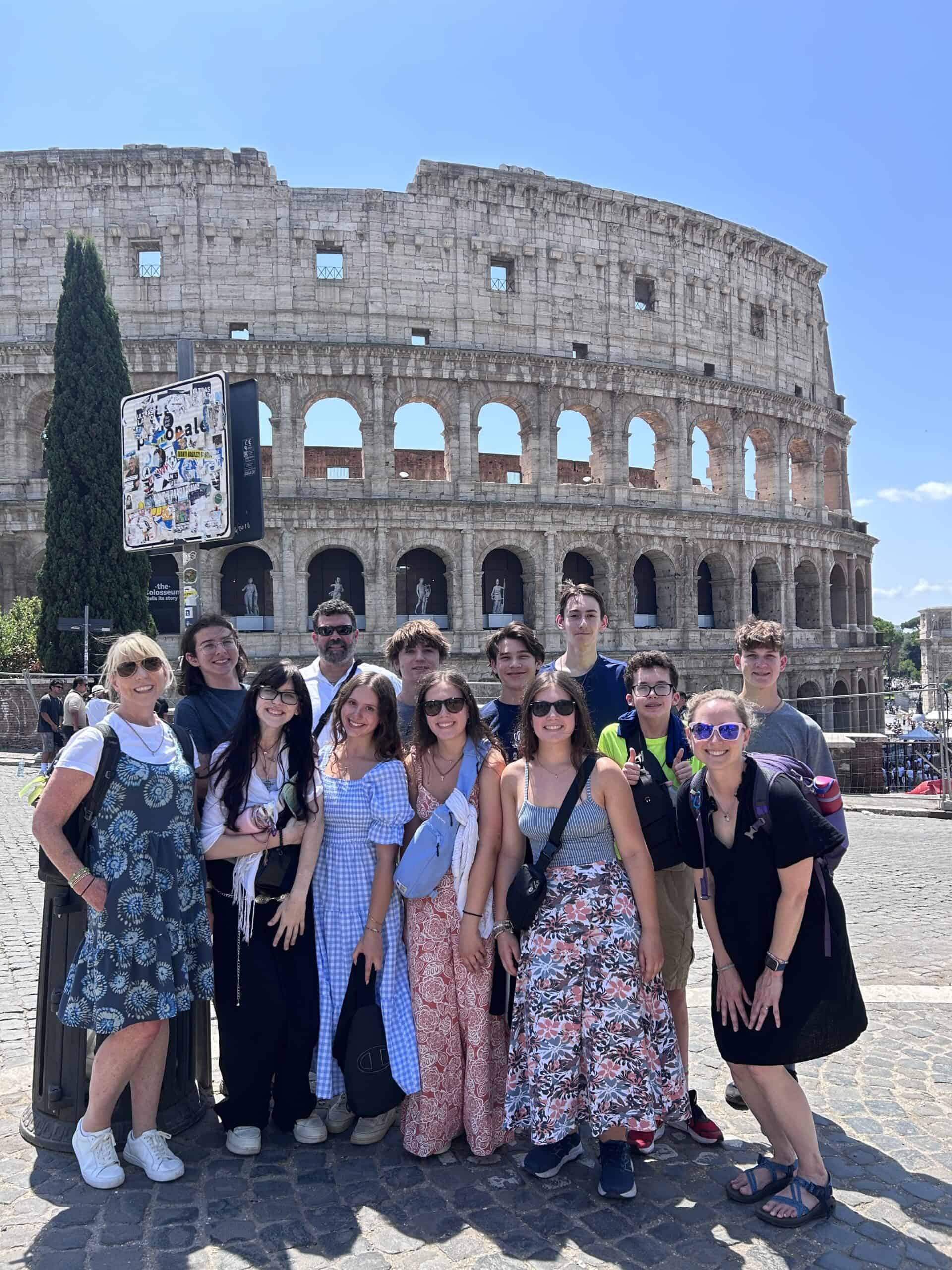 A group of people posing in front of the Colosseum in Rome, Italy, under a clear blue sky.